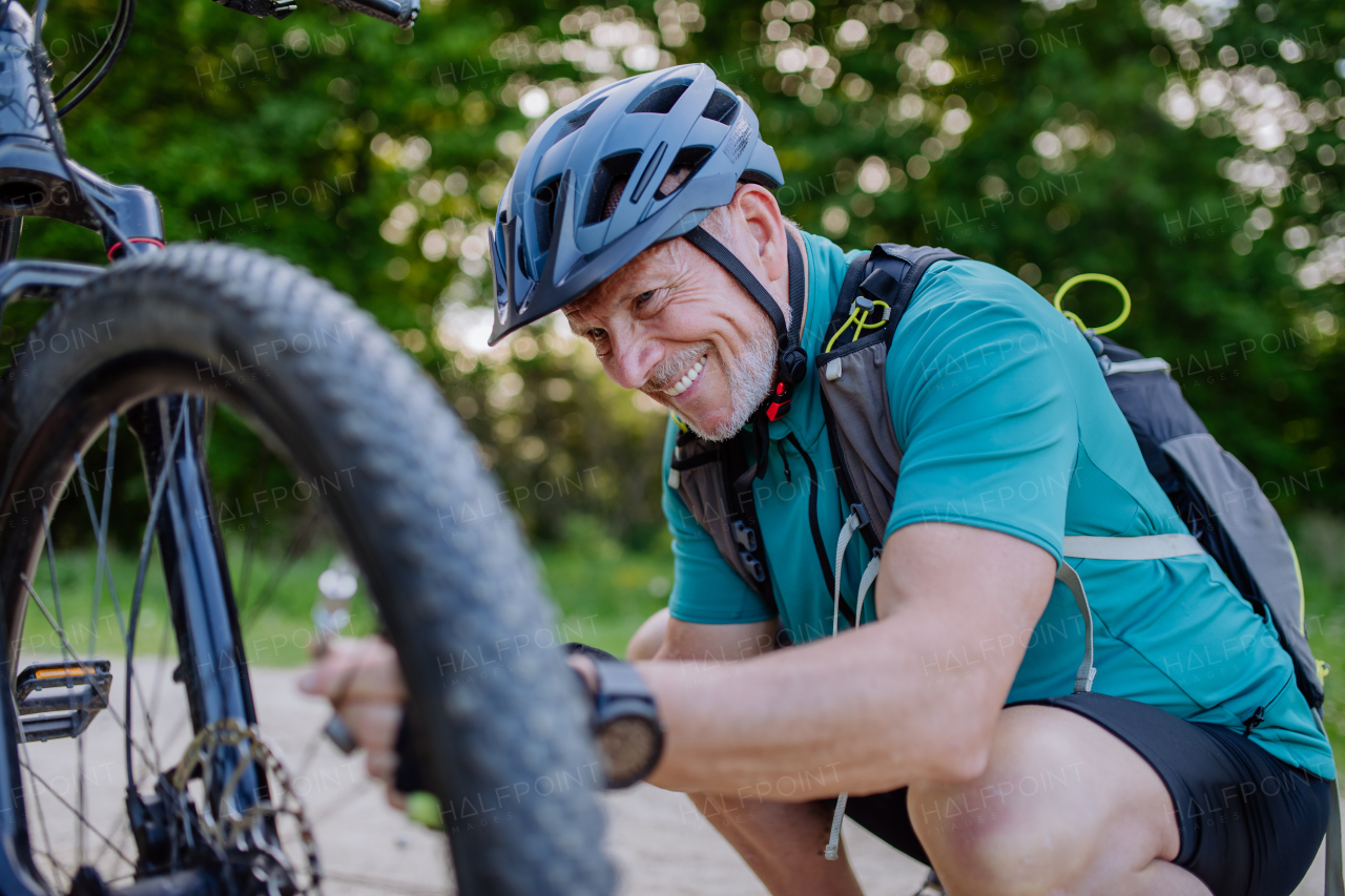 An active senior man repairing bicycle, pumping up tire in nature in summer.