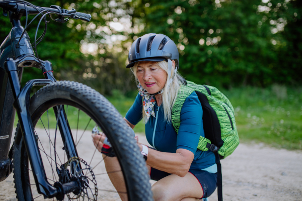 An active senior woman repairing bicycle, pumping up tire in nature in summer.