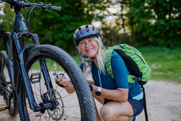 An active senior woman repairing bicycle, pumping up tire in nature in summer.