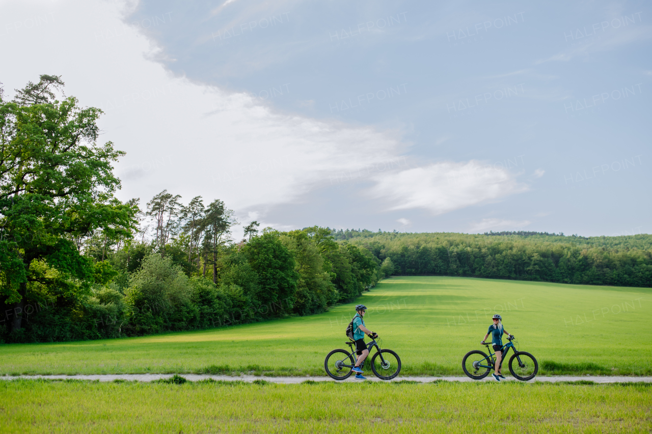 An active senior couple riding electric bicycles on path at summer park, healthy lifestyle concept.