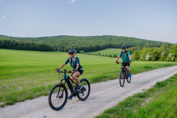 An active senior couple riding electric bicycles on path at summer park, healthy lifestyle concept.