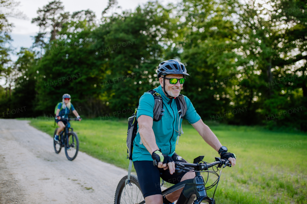 An active senior couple riding electric bicycles on path at summer park, healthy lifestyle concept.