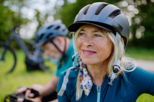 An active senior couple riding bicycles at summer park, woman with bicycle helmet, healthy lifestyle concept.