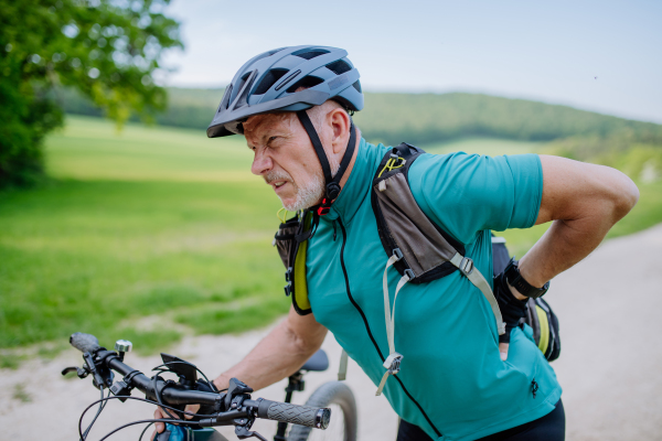 An active senior man in sportswear suffiering from pain in his back after cycling, in park in summer.