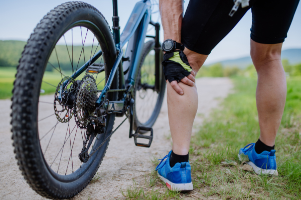 A close-up of active senior man in sportswear suffiering from pain in his knee after cycling, in park in summer.