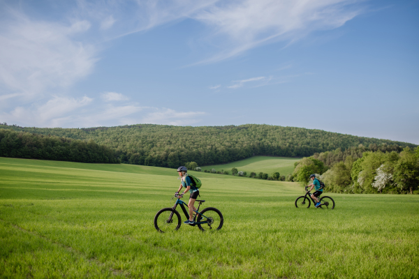 An active senior couple riding electric bicycles on path at summer park, healthy lifestyle concept.