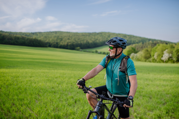 An active senior man with electric bicycles on meadow in summer, healthy lifestyle concept.