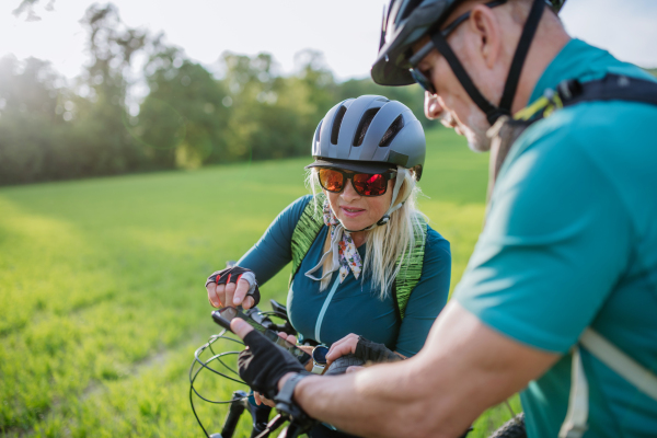 An active senior couple resting after bicycle ride at summer park, using smartphone.