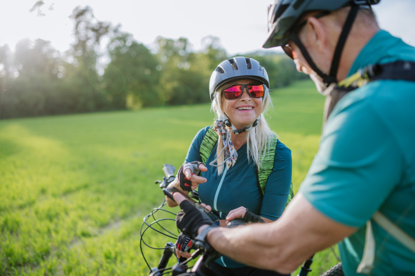 An ctive senior couple riding electric bicycles on road at summer park, healthy lifestyle concept.