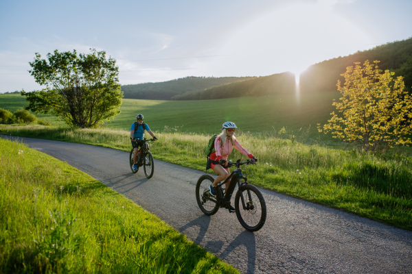 An ctive senior couple riding electric bicycles on road at summer park, healthy lifestyle concept.