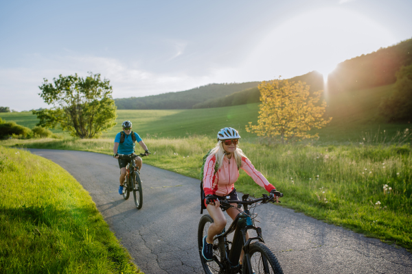 An ctive senior couple riding electric bicycles on road at summer park, healthy lifestyle concept.