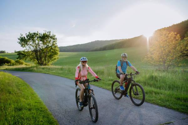 An ctive senior couple riding electric bicycles on road at summer park, healthy lifestyle concept.