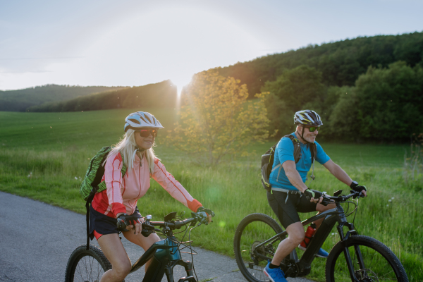 An active senior couple riding electric bicycles on path at summer park, healthy lifestyle concept.