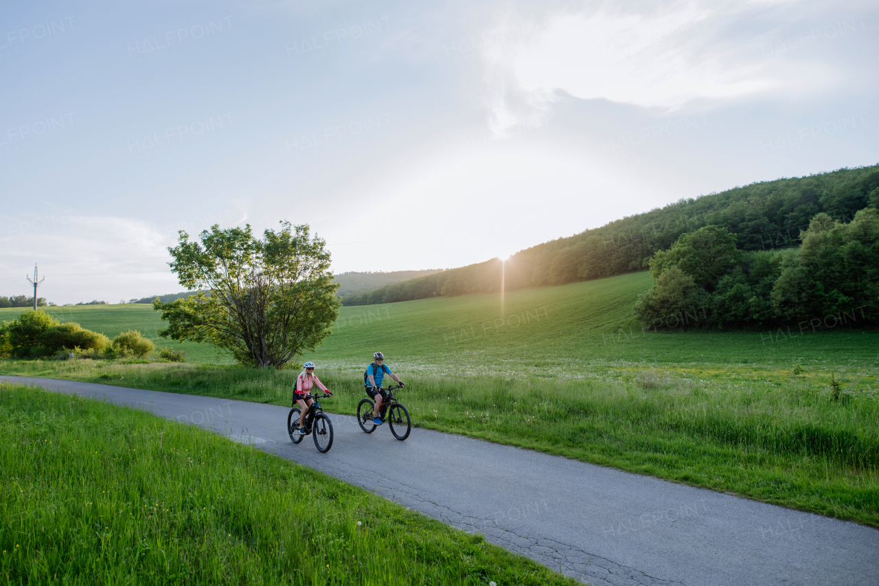 An active senior couple riding electric bicycles on path at summer park, healthy lifestyle concept.