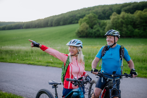 An ctive senior couple riding electric bicycles on road at summer park, healthy lifestyle concept.