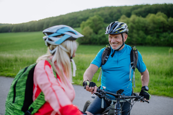 An ctive senior couple riding electric bicycles on road at summer park, healthy lifestyle concept.