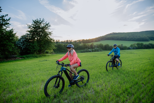 An active senior couple riding electric bicycles on path at summer park, healthy lifestyle concept.