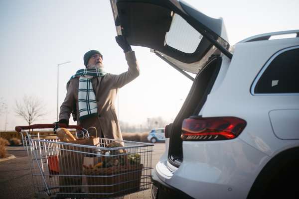 Senior man giving his purchase in the electric car trunk.