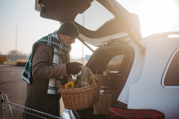 Senior man giving his purchase in the electric car trunk.