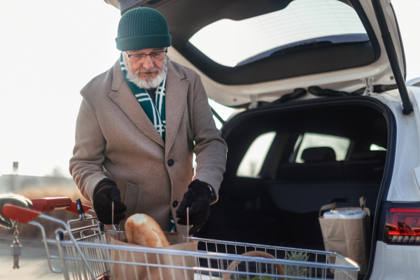 Senior man giving his purchase in the electric car trunk.