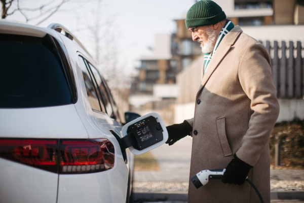 Close up of a senior man charging electric car.