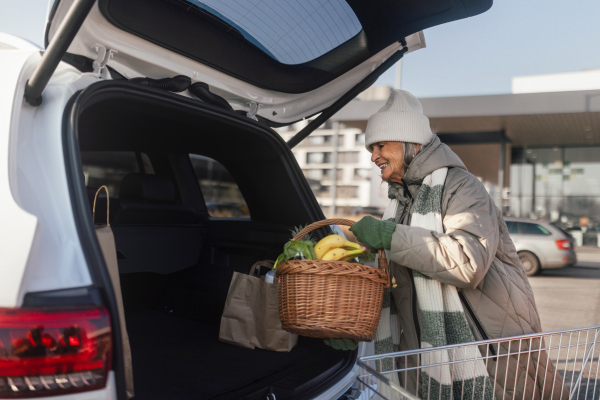 Senior woman giving his purchase in the electric car trunk.