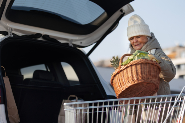 Senior woman giving his purchase in the electric car trunk.