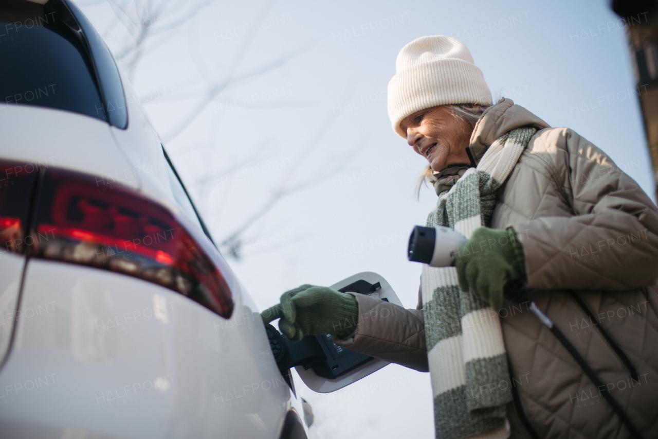 Close up of a senior woman charging electric car.