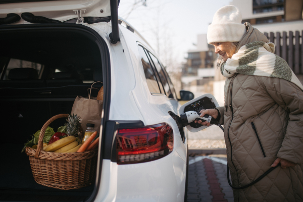 Close up of a senior woman charging electric car.