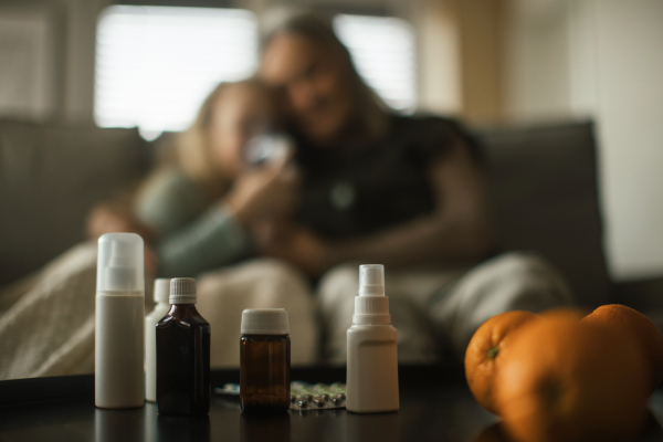 Close-up of medicines, grandmother taking care of her sick granddaughter in a background.