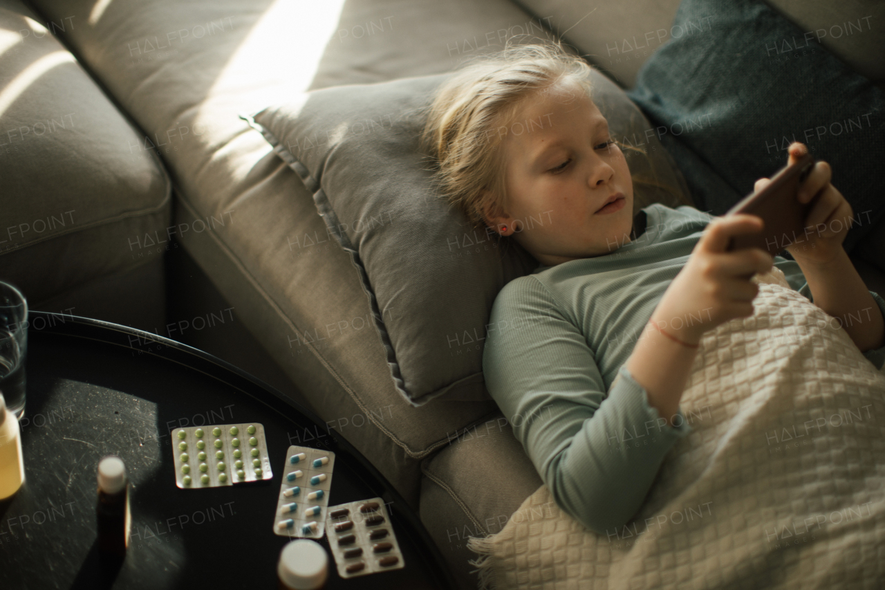 Little sick girl lying in a bed and scrolling her phone.