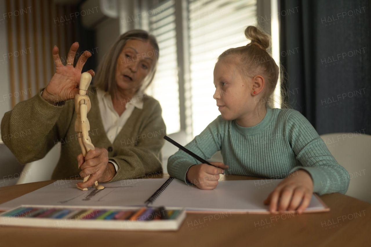 Senior woman teaching her little granddaughter figural drawing.