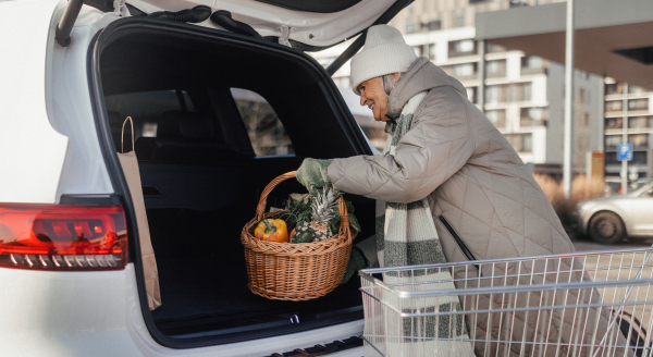 Senior woman giving his purchase in the electric car trunk.