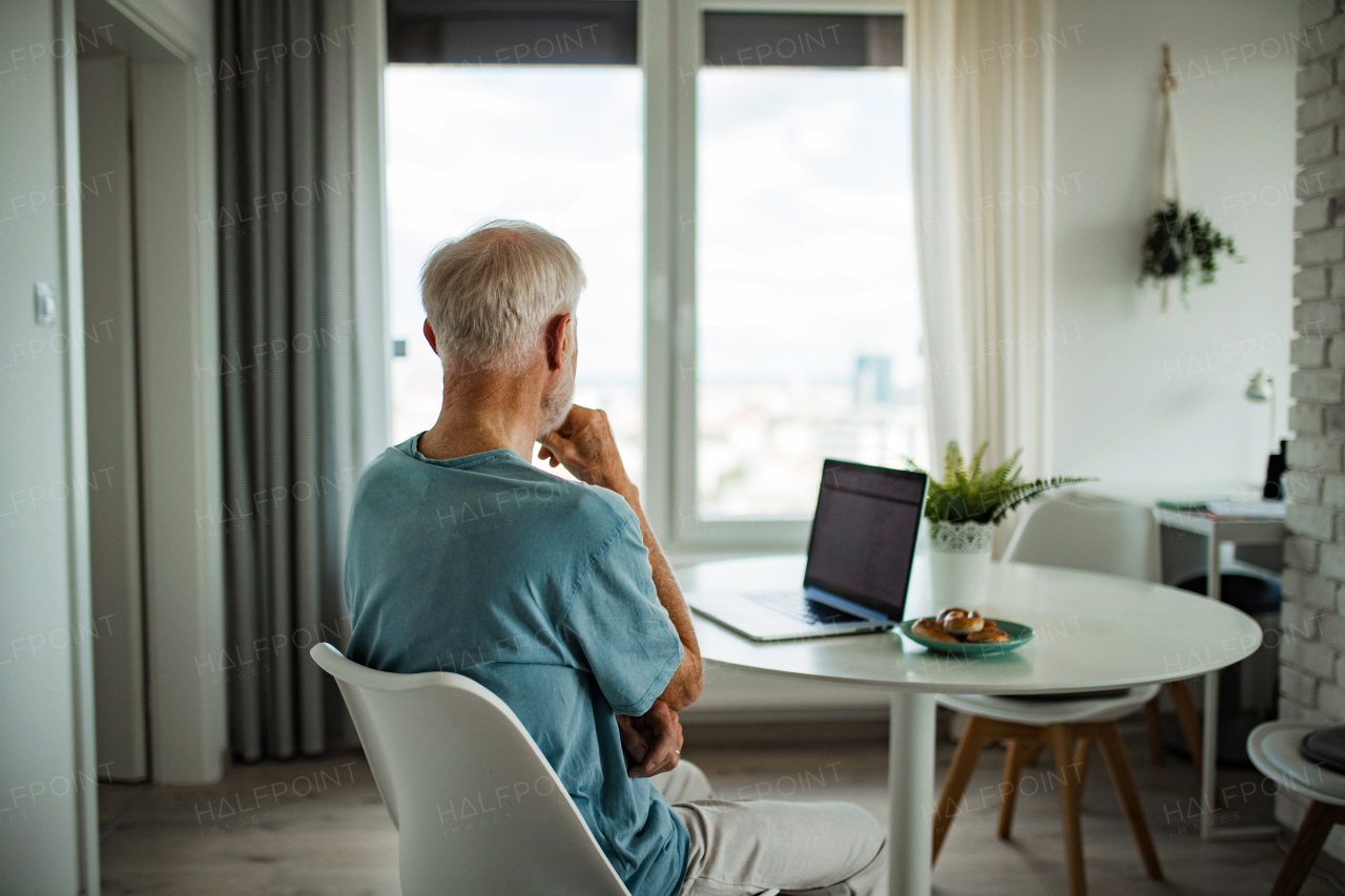 Senior man in a wheelchair working from home during retirement. Elderly man using digital technologies, working on a laptop. Concept of seniors and digital skills.