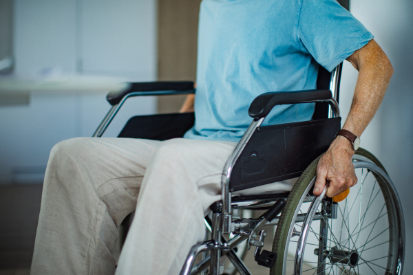 Close-up of an senior man sitting in a wheelchair. The elderly man is sitting in the wheelchair at home, holding the wheels with his hands.