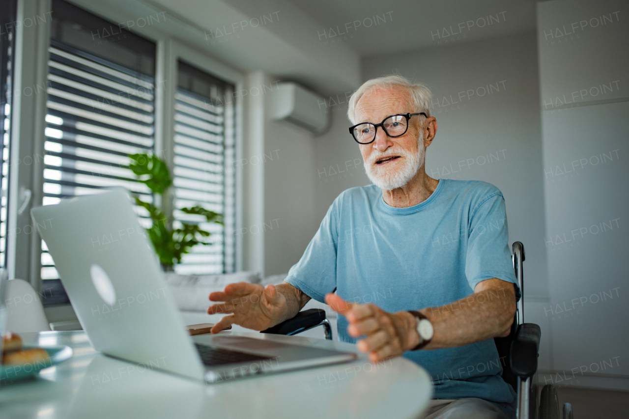 Senior man in wheelchair shopping online on laptop. Online financial scam targetin older people. Concept of seniors and digital skills.