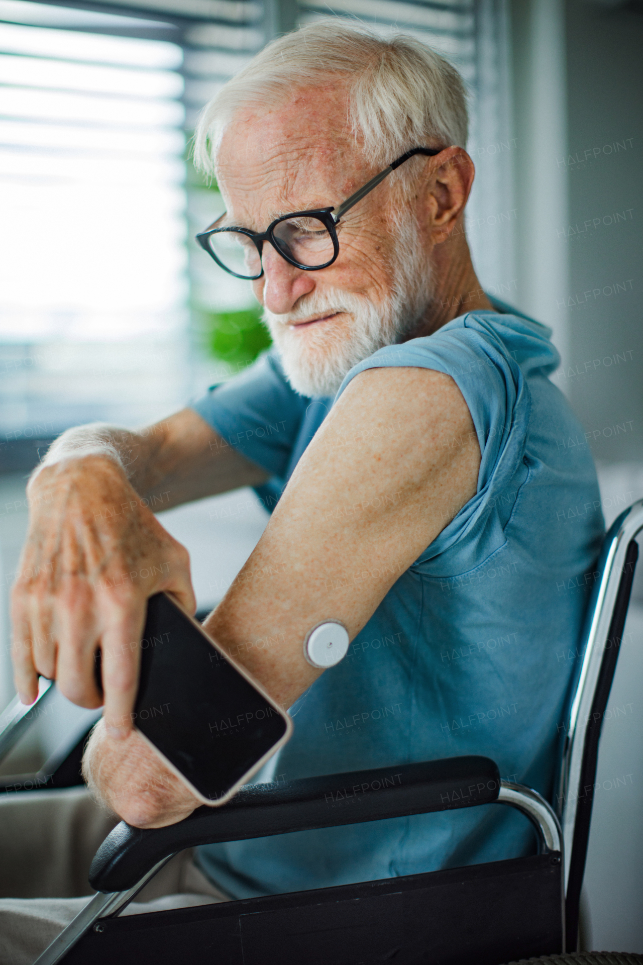 Diabetic senior man checking blood glucose level at home using continuous glucose monitor. Elderly man connecting his CGM with smarphone to see blood sugar levels in real time.