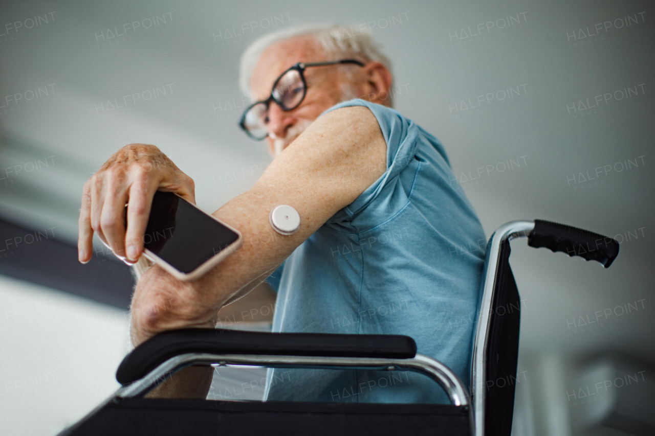 Diabetic senior man checking blood glucose level at home using continuous glucose monitor. Elderly man connecting his CGM with smarphone to see blood sugar levels in real time.