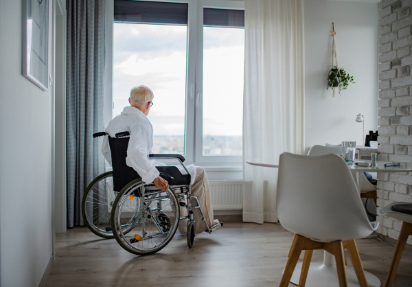 Senior man in a wheelchair spending time alone in his apartment. Concept of loneliness and dependence of retired people.