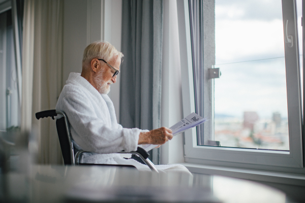 Elderly man in a wheelchair reading the newspaper in his robe in the morning. Concept of loneliness and dependence of retired people.