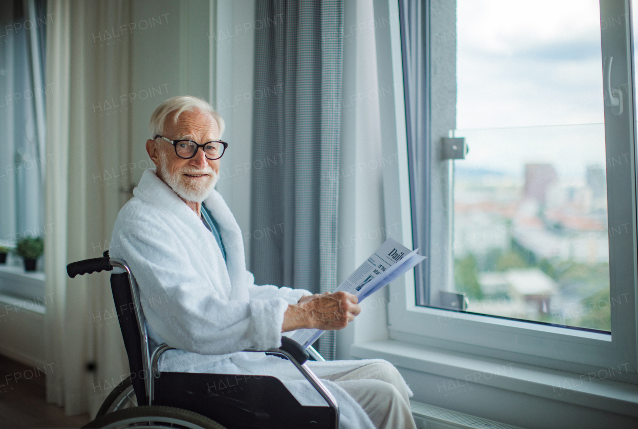 Elderly man in a wheelchair reading the newspaper in his robe in the morning. Concept of loneliness and dependence of retired people.