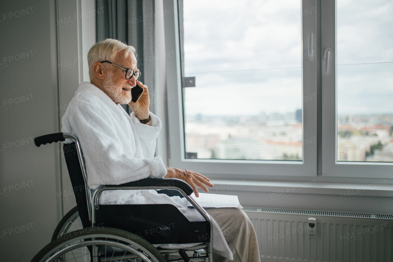 Elderly man in a wheelchair making call in his robe in the morning. Concept of loneliness and dependence of retired people.