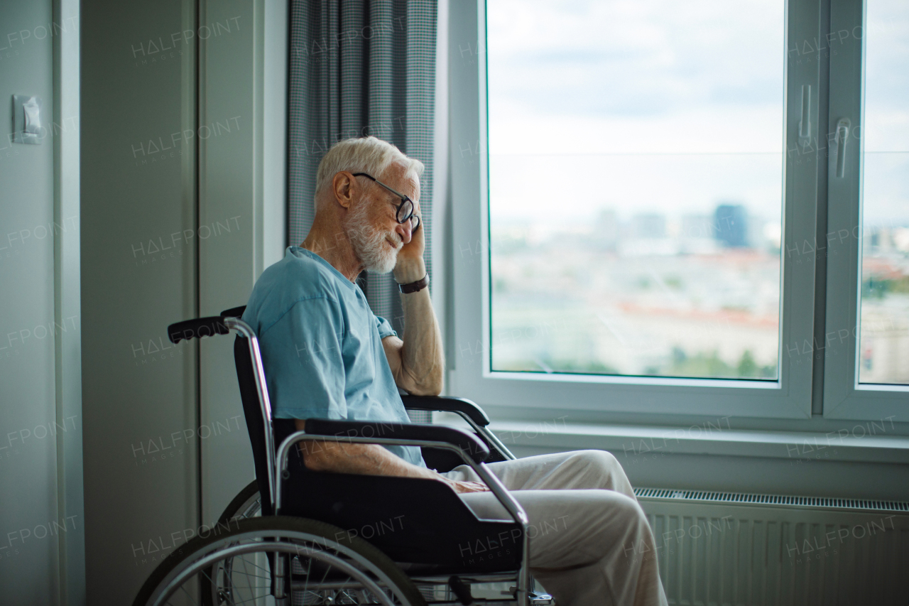 Senior man in a wheelchair spending time alone in his apartment. Concept of loneliness and dependence of retired people.