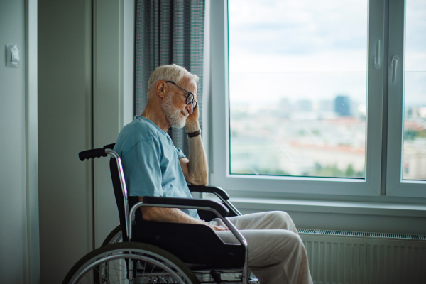 Senior man in a wheelchair spending time alone in his apartment. Concept of loneliness and dependence of retired people.