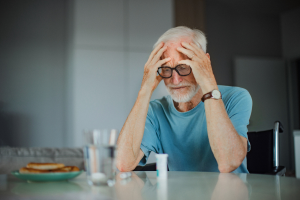 Portrait of senior man in wheelchair taking pills at home, he is confused about mediacation usage. Chronically ill man have no money for his medication.