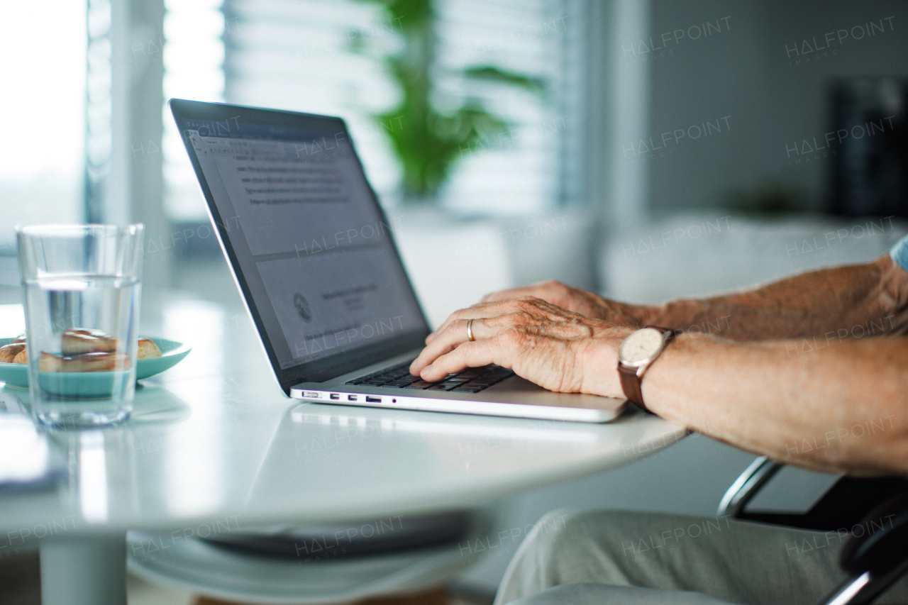 Close-up shot of the hands of an elderly man typing on a laptop keyboard. Concept of working from home.