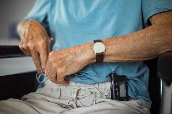 Senior man checking his blood sugar level on an insulin pump. Close up of senior man in wheelchair with type 1 diabetes.