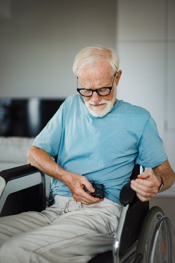 Senior man checking his blood sugar level on an insulin pump. Close up of senior man in wheelchair with type 1 diabetes.