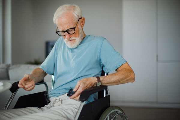 Senior man checking his blood sugar level on an insulin pump. Close up of senior man in wheelchair with type 1 diabetes.