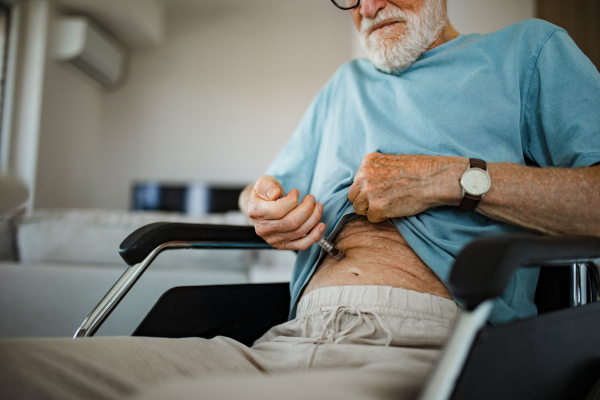 Diabetic senior patient injecting insulin in his belly. Close up of senior man in wheelchair with type 1 diabetes taking insuling with syringe needle.